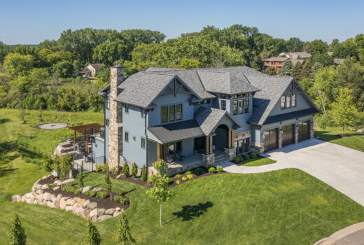 Drone view of a blue exterior home surrounded by lush green trees and a well-kept lawn. A beautiful residential project completed by Allied Construction.