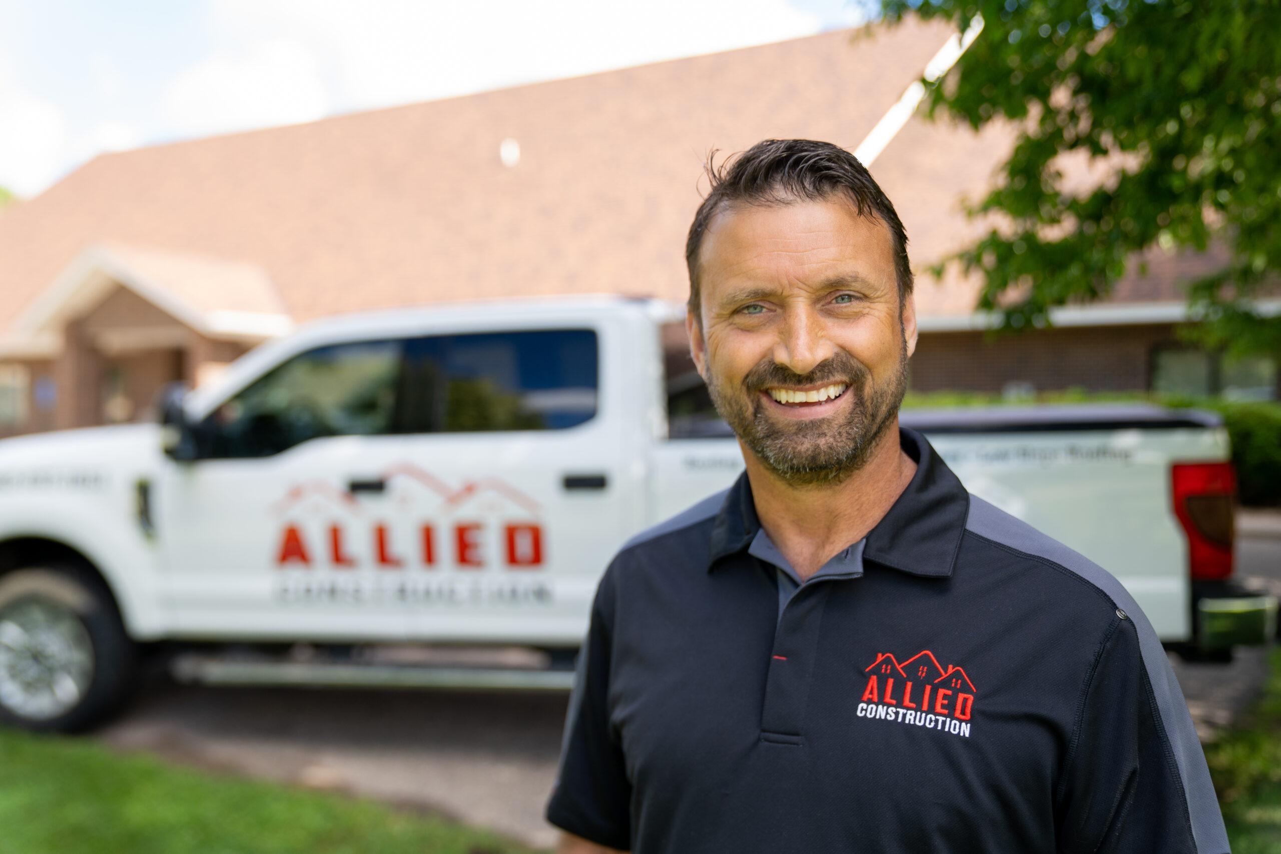 Smiling Allied Construction team member standing in front of branded truck