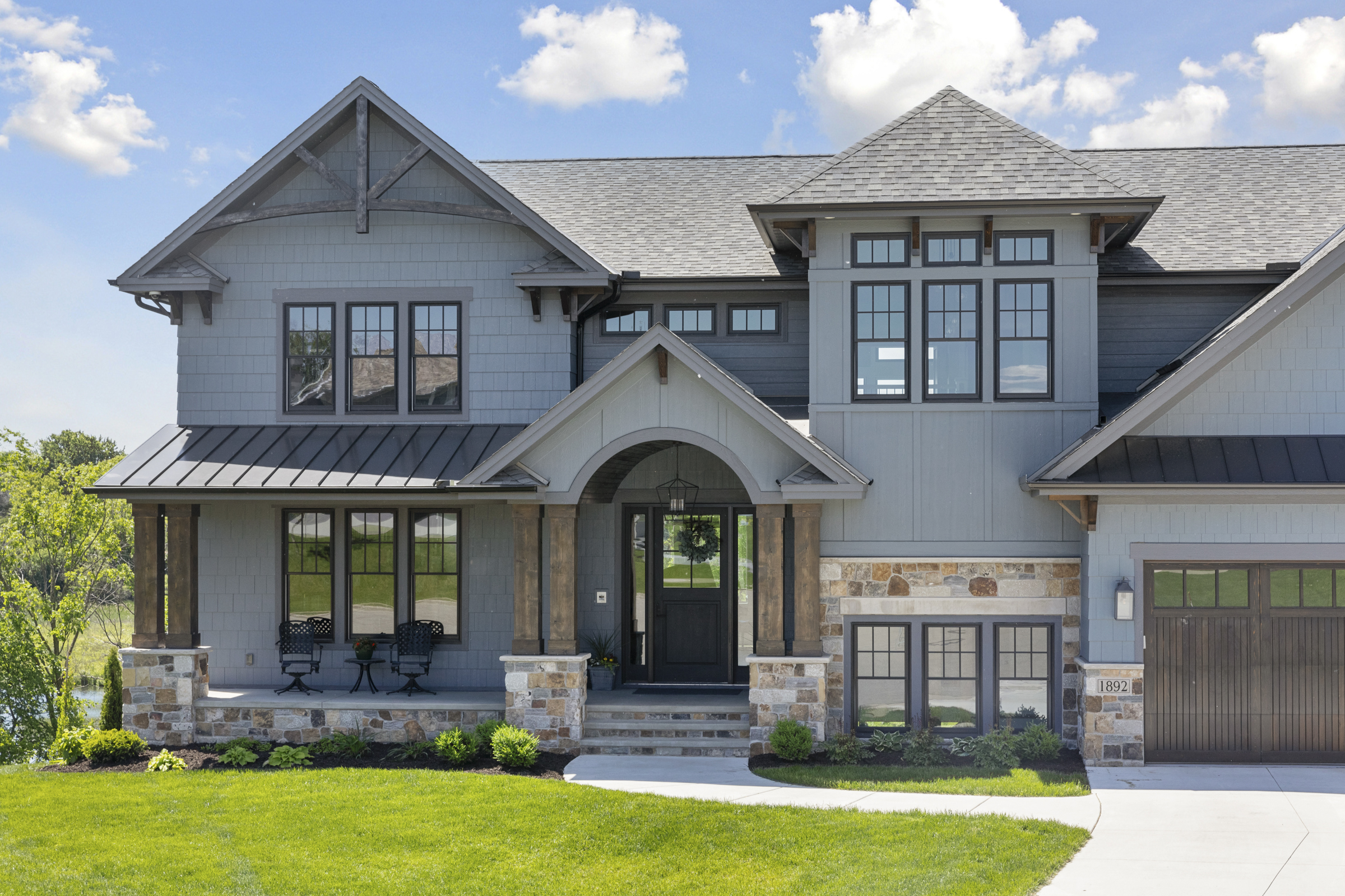 Front view of a custom home with new asphalt shingle roofing, black-framed windows, and stone accents