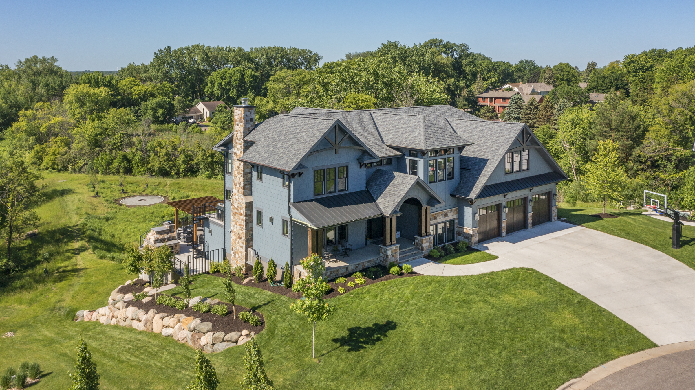Drone view of a blue exterior home surrounded by lush green trees and a well-kept lawn. A beautiful residential project completed by Allied Construction.