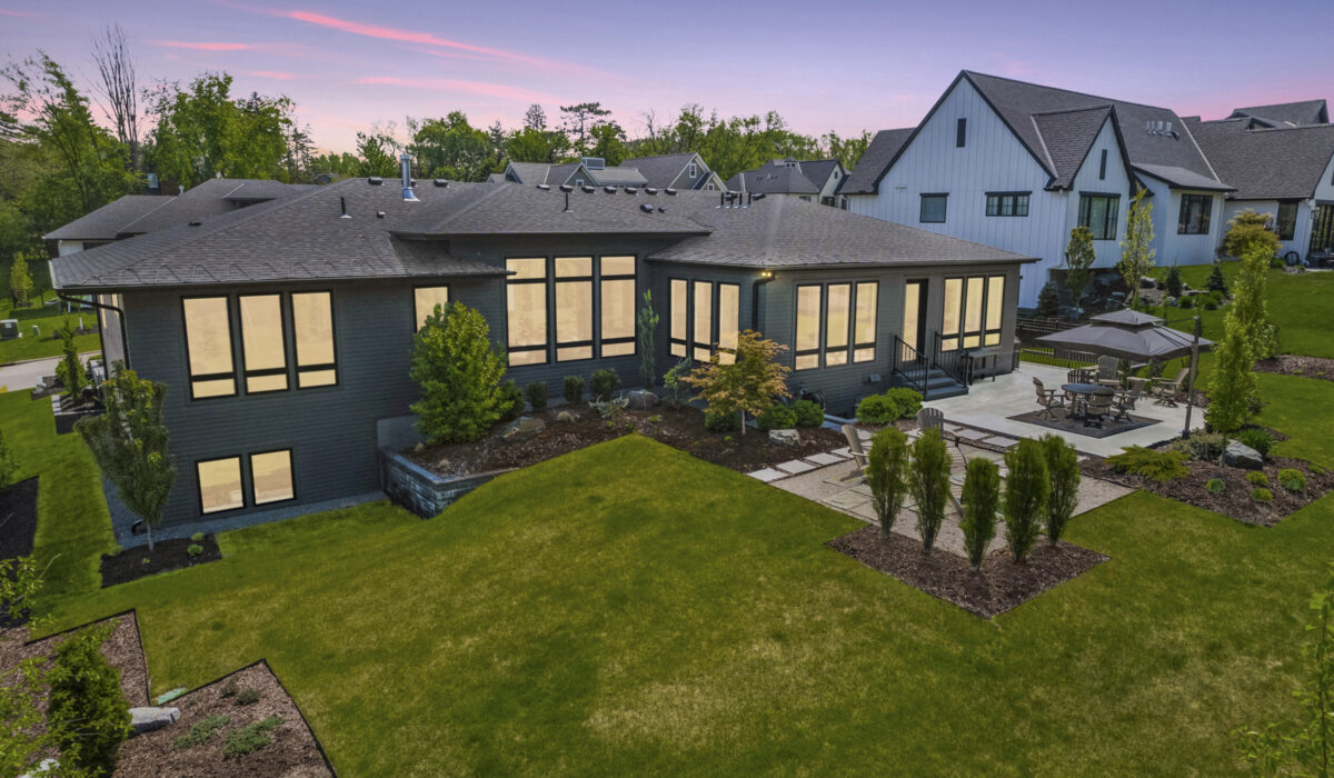 Evening view of roofing on modern home with illuminated windows and patio.