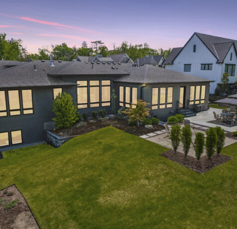 Evening view of roofing on modern home with illuminated windows and patio.