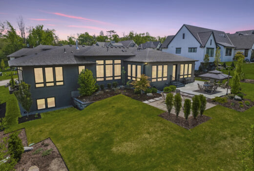 Evening view of roofing on modern home with illuminated windows and patio.