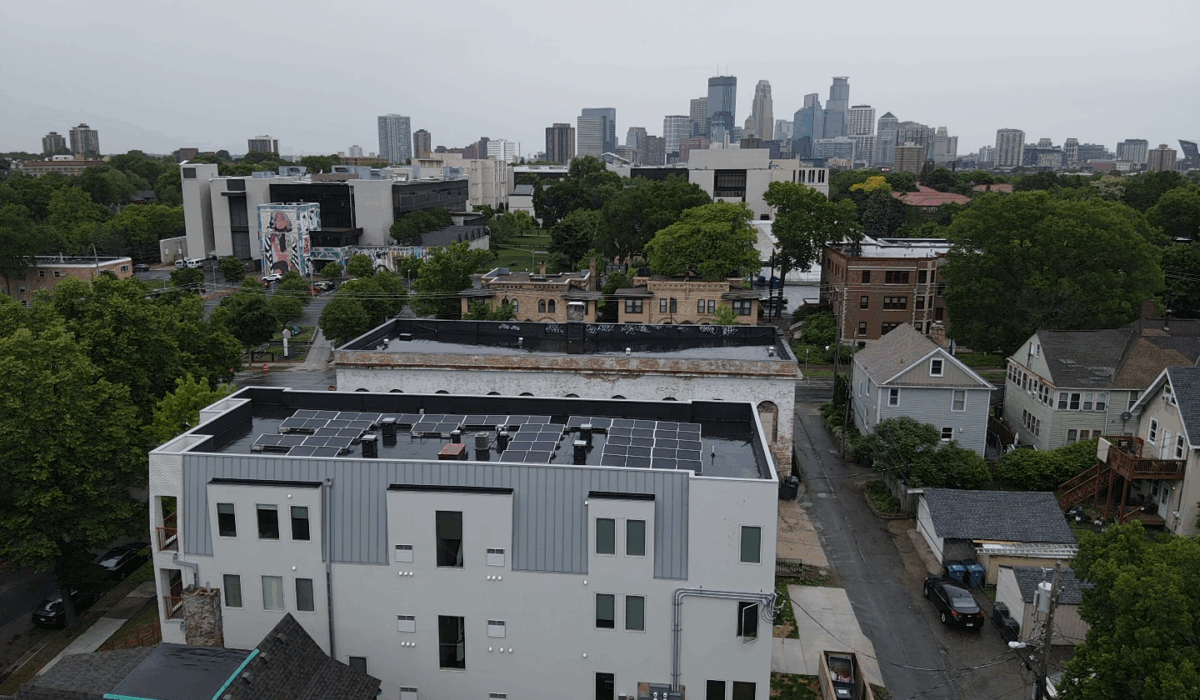 Aerial view of flat roof installation on a Minneapolis building with solar panels and city skyline in the background.