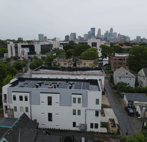 Aerial view of flat roof installation on a Minneapolis building with solar panels and city skyline in the background.