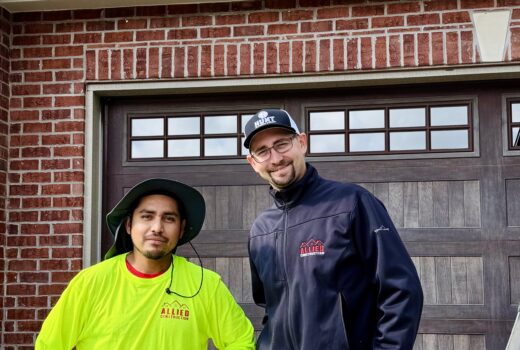 Two Allied Construction team members standing in front of a brick home and garage, smiling at the camera.