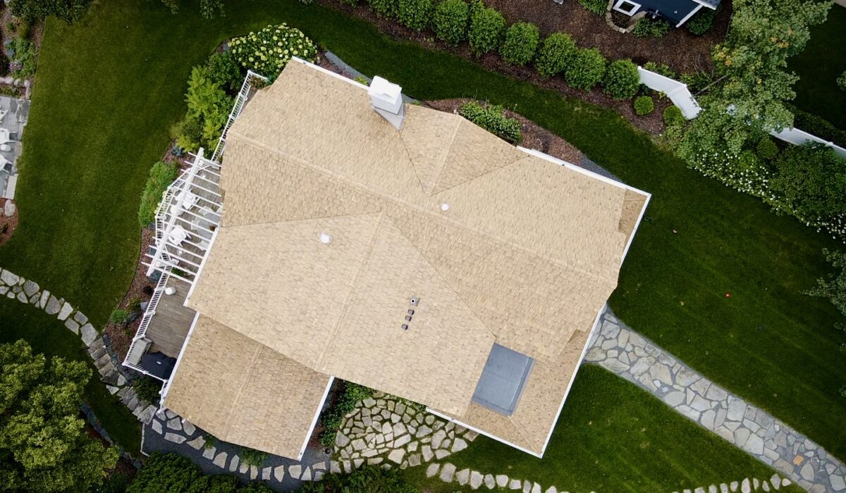 The front of the lakeside home featuring a newly installed Brava shake roof, gray shingle siding, white trim, and a decorative balcony planter.