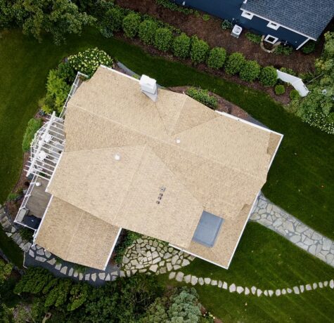The front of the lakeside home featuring a newly installed Brava shake roof, gray shingle siding, white trim, and a decorative balcony planter.