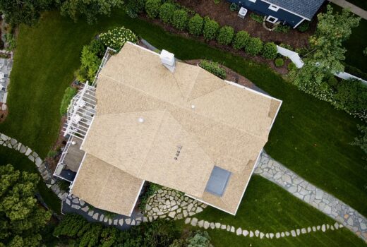 The front of the lakeside home featuring a newly installed Brava shake roof, gray shingle siding, white trim, and a decorative balcony planter.